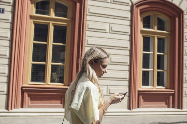 Mujer rubia joven caminando y usando el teléfono celular — Foto de Stock