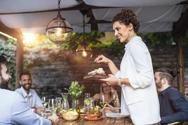 Dîner de femme hôte de fête servant de la nourriture à ses amis — Photo