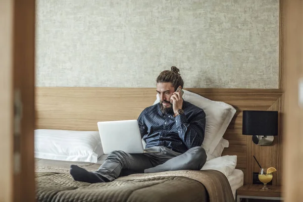 Handsome Caucasian Businessman Sitting Hotel Bed Talking Phone Typing Laptop — Stock Photo, Image