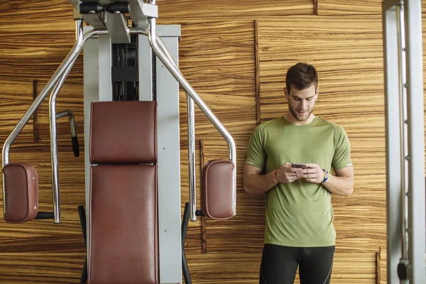英俊的白种运动员在健身房输入智能手机 — 图库照片