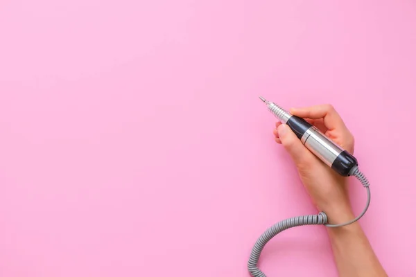 Kadın elinde elektrikli çivi manikür makinesi olan pembe arka planda bir kalem tutuyor.