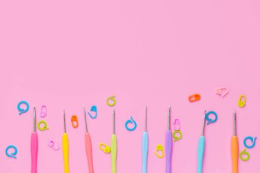 Pembe arka planda renkli örgü aksesuarları olan farklı boyutlarda örgü kancaları