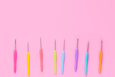 Pembe arka planda çeşitli boyutlarda parlak örgü kancaları