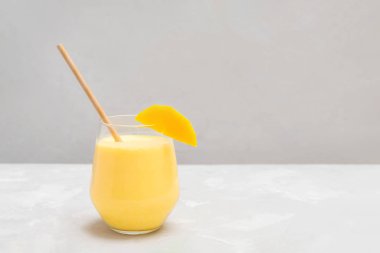 Geleneksel Hint içkisi, gri beton arka planda kağıt kamışla cam bir fincanda Mango Lassi.