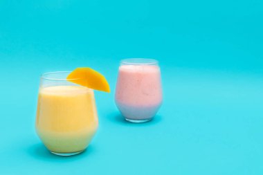 Mango Lassi ve Çilek Lassi mavi arka planda cam bardaklarda içki içerler.