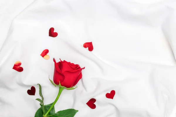 Above view of red rose with shiny hearts on white bed sheets. Image with copy space, flat lay. — Stock Photo, Image