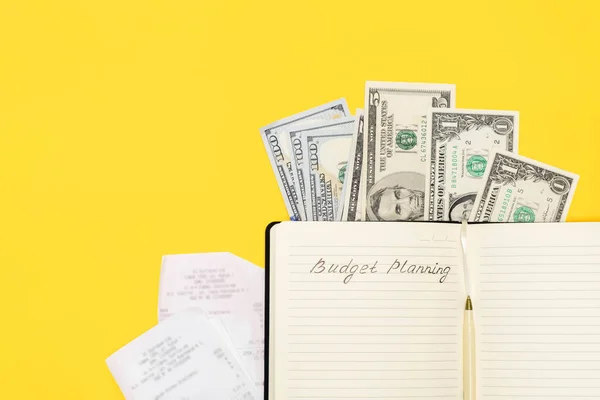 Directly above view of money, bills, pen and notepad with handwritten words Budget Planning on yellow background, copy space. Personal Expense Calculation concept.