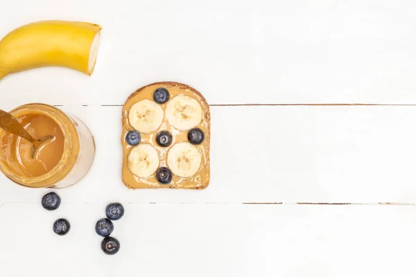 Breakfast toasts. Peanut butter toast with blueberry and banana on white wooden table.