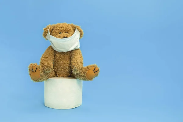 Teddybär trägt Mundschutz und sitzt auf einer Toilettenpapierrolle auf blauem Hintergrund — Stockfoto