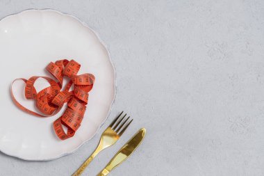 Diyet konsepti. Tarafsız zemin üzerinde mezura ve altın çatal bıçak ile boş beyaz tabak metin için yer, düz yatıyordu