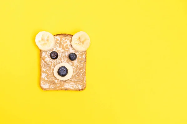 面白い子供たちは 黄色の背景にブルーベリーとバナナとクマの形でピーナッツバターと朝食トースト トップビュー コピースペース — ストック写真