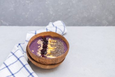 Muz, chia ve ayçiçeği tohumlarıyla dolu böğürtlen suyu kasesi doğal bir hindistan cevizi kasesinde nötr gri masa üzerinde metin için yer var.