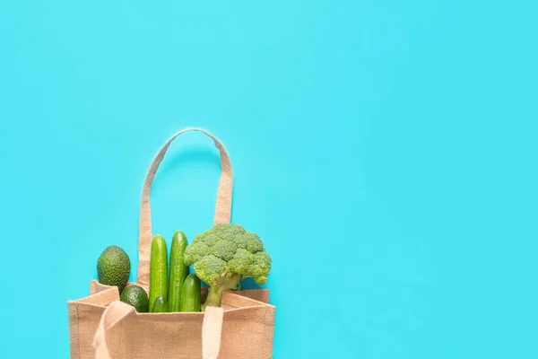 Green vegetables in eco-friendly recycled shopping bag on blue background. Top view, flat lay, copy space