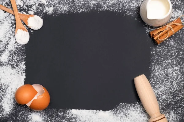 Baking ingredients on black background. Eggshells, rolling pin, flour, milk and spices. Home baking concept, baking cake or cookies ingredients. Background layout with free text space.