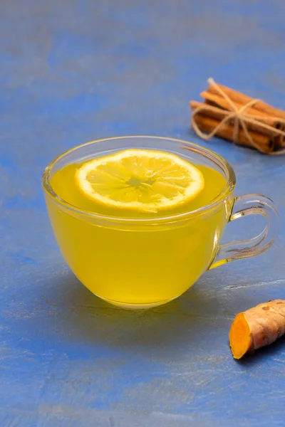 Daily detox lemon, ginger and turmeric tea in a glass cup on blue background