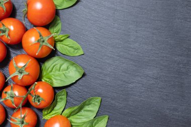 Koyu arkaplanda yeşil yapraklı ve sarımsaklı taze kırmızı domatesler.