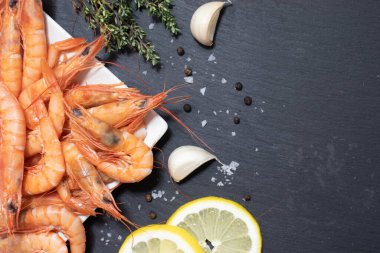 Lezzetli kırmızı haşlanmış karides, limon, sarımsak, tuz ve biber ve kara tahtada otlar..