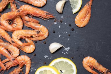 Lezzetli kırmızı haşlanmış karides, limon, sarımsak, tuz ve biber ve kara tahtada otlar..