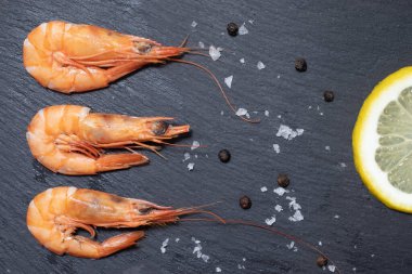 Lezzetli kırmızı haşlanmış karides, limon, sarımsak, tuz ve biber ve kara tahtada otlar..