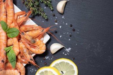 Lezzetli kırmızı haşlanmış karides, limon, sarımsak, tuz ve biber ve kara tahtada otlar..
