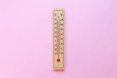 Pembe arka planda klasik bir ahşap termometre 20 derece sıcaklık ve 70 derece fahrenhayt gösteriyor.