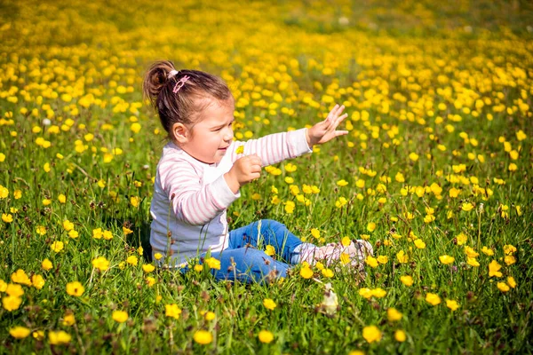 Chica joven sentada en el prado, extendiendo la mano, fondo borroso — Foto de Stock