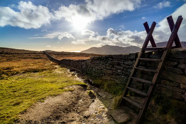 Mourn Wall met ladder aan de oever van de Slieve Donard berg met blauwe lucht, witte wolken en zonnestralen — Stockfoto