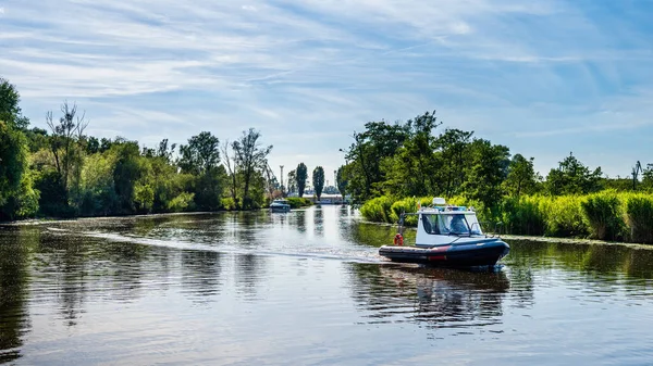 Motor inflatable boat floats on a river, surrounded by river reeds and tries, beautiful summer day on Szczecin yacht marina, Poland