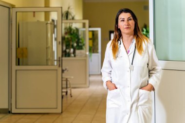 Orta yaşlı, beyaz, beyaz, kadın doktor boş bir hastane koridorunda hastaların koronavirüs ya da covid 19 aşısı yapmasını bekliyor.