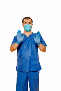 Önlüklü, koruyucu maskeli ve eldivenli erkek doktor her iki elinde ve avucunda dur işareti var. Düz beyaz arkaplan Coronavirus kavramı