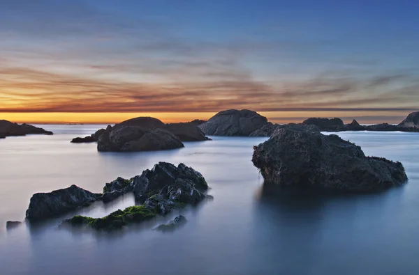 Sonnenuntergang am Strand mit blauem Wasser und Felsen — Stockfoto