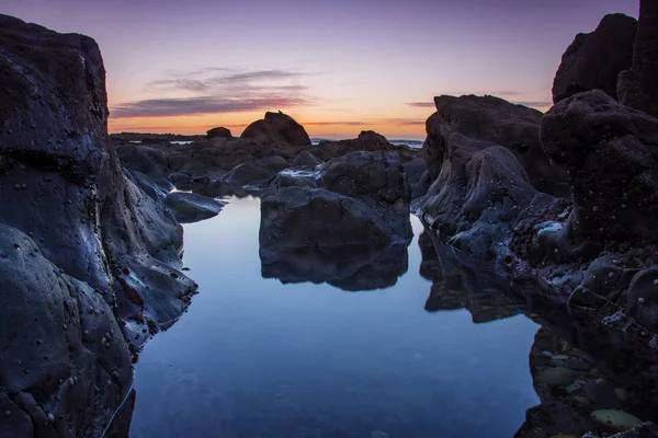 Strand mit Felsen und blauem Wasser bei Sonnenuntergang — Stockfoto