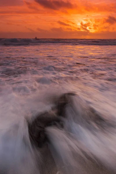 Roter Sonnenuntergang am Strand mit starken Wellen und einem Schiff im Ozean — Stockfoto