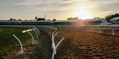 Arka planda günbatımı olan at yarışı sahası