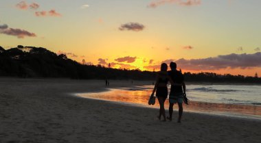 Gün batımında sahilde yürüyen bir çift.