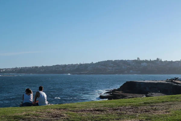 Pareja sentada en la hierba con vistas al mar y a la ciudad — Foto de Stock