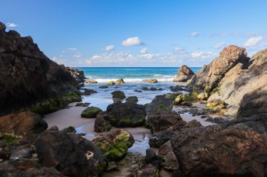 Arka planda birkaç kaya ve okyanus olan ücra bir koy.