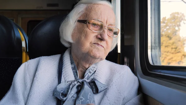 Starsza pani patrzy przez okno w pociągu. — Zdjęcie stockowe