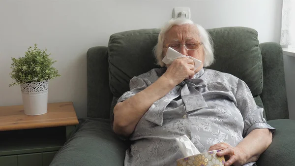 Старая больная женщина держит коробку с бумажными салфетками и кашляет. — стоковое фото