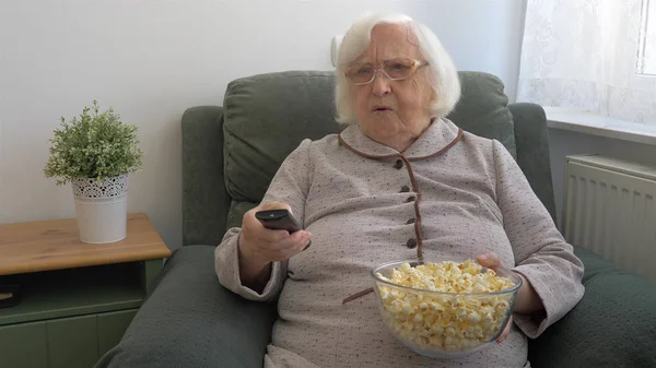 Stará žena s miskou popcornu se dívá na televizi — Stock fotografie