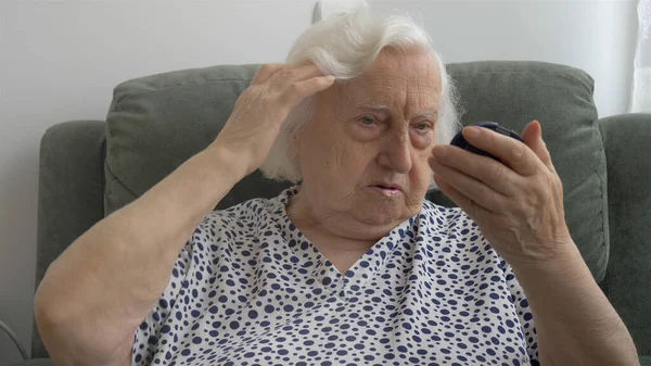 Mujer mayor corrige su cabello y se mira en el espejo — Foto de Stock