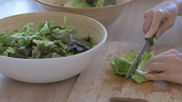 La mujer está cortando hojas de lechuga en una tabla de cortar para una ensalada — Foto de Stock