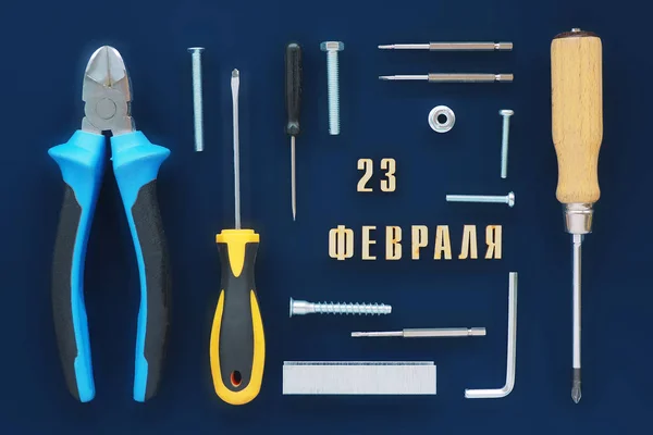 Greeting card. male tools, wire cutters, screwdrivers, wrenches, bolts, staples for a stapler, screws, nuts, and an inscription in Russian from February 23 on a dark blue background