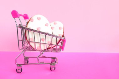 İki yumurta şeklinde zencefilli kurabiye ve pembe arka planda kalpleri olan küçük bir alışveriş arabası. Paskalya indirimi