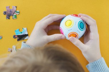 Çocuk, içinde renkli toplar olan bir yapboz ve sarı arka planda bir mukavva yapbozun ayrıntılarıyla meşgul.