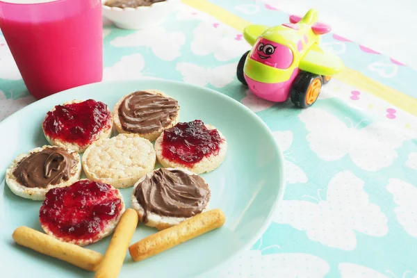 Food art idea. Wheat round bread rolls with jam and chocolate paste in the shape of a flower on a blue plate. Milk and a toy
