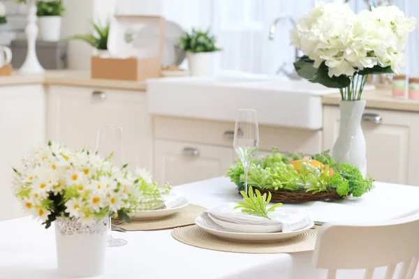 Served dining table with a white tablecloth, flowers, glasses and plates. sink by the window.