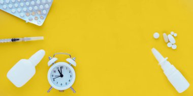 Burun spreyi, haplar, çalar saat ve sarı arka planda şırınga. Mevsimsel soğuk algınlığı kavramı