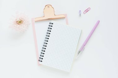Bir yay üzerinde açık bir defter, pembe bir pano, kalem, ataç ve beyaz bir masada kasımpatı çiçeği. Metin için boşluk