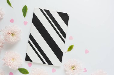 siyah ve beyaz defterler ve bir sürü pembe kasımpatı çiçekleri ve beyaz bir masada yeşil yapraklar. Metin için boşluk